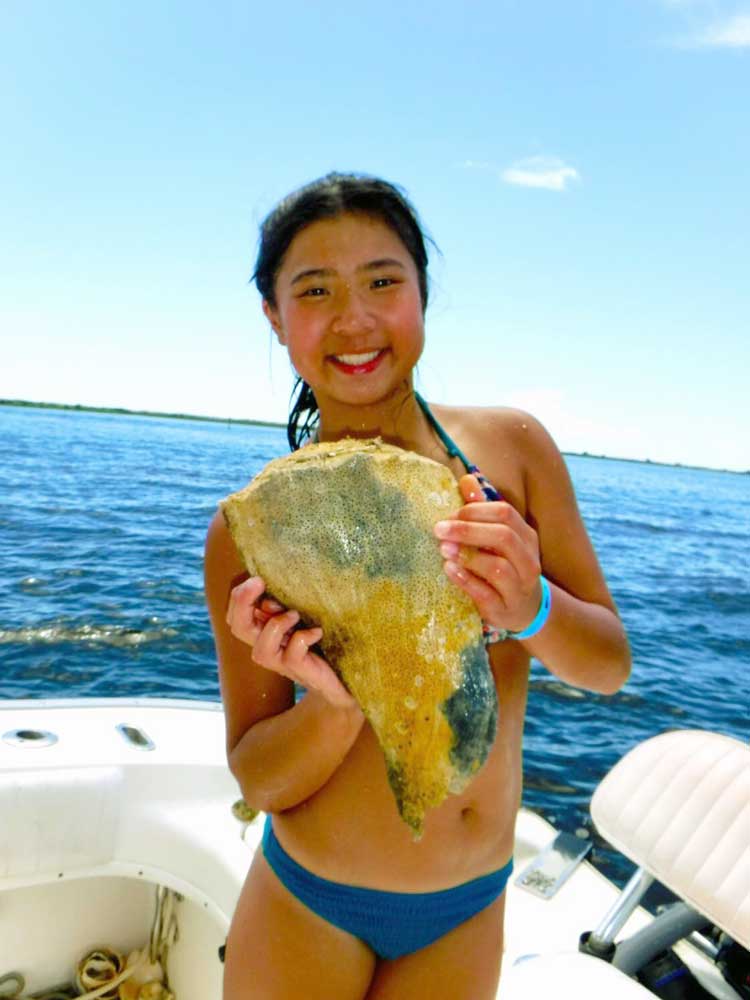 Girl holding conch shell while standing on Pontoon boat rental