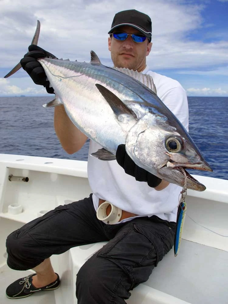 Man sitting on edge of boat holding up big tuna he caught on his fishing charter