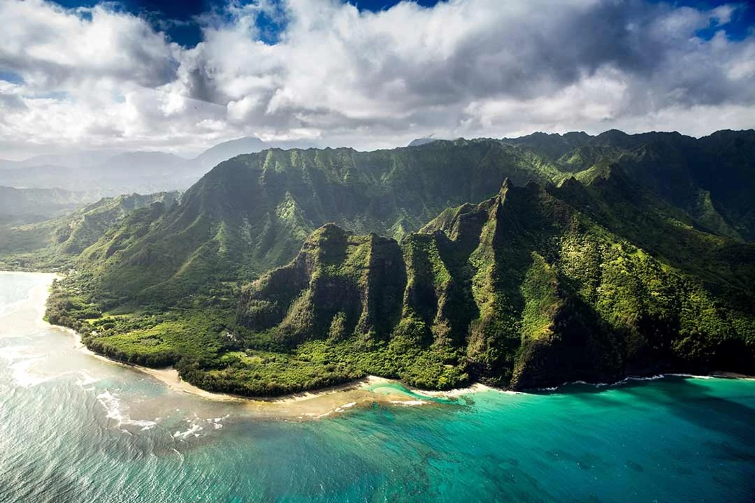 Aerial view of the beach, beautiful aqua waters, and steep cliffs of green in Hawaii