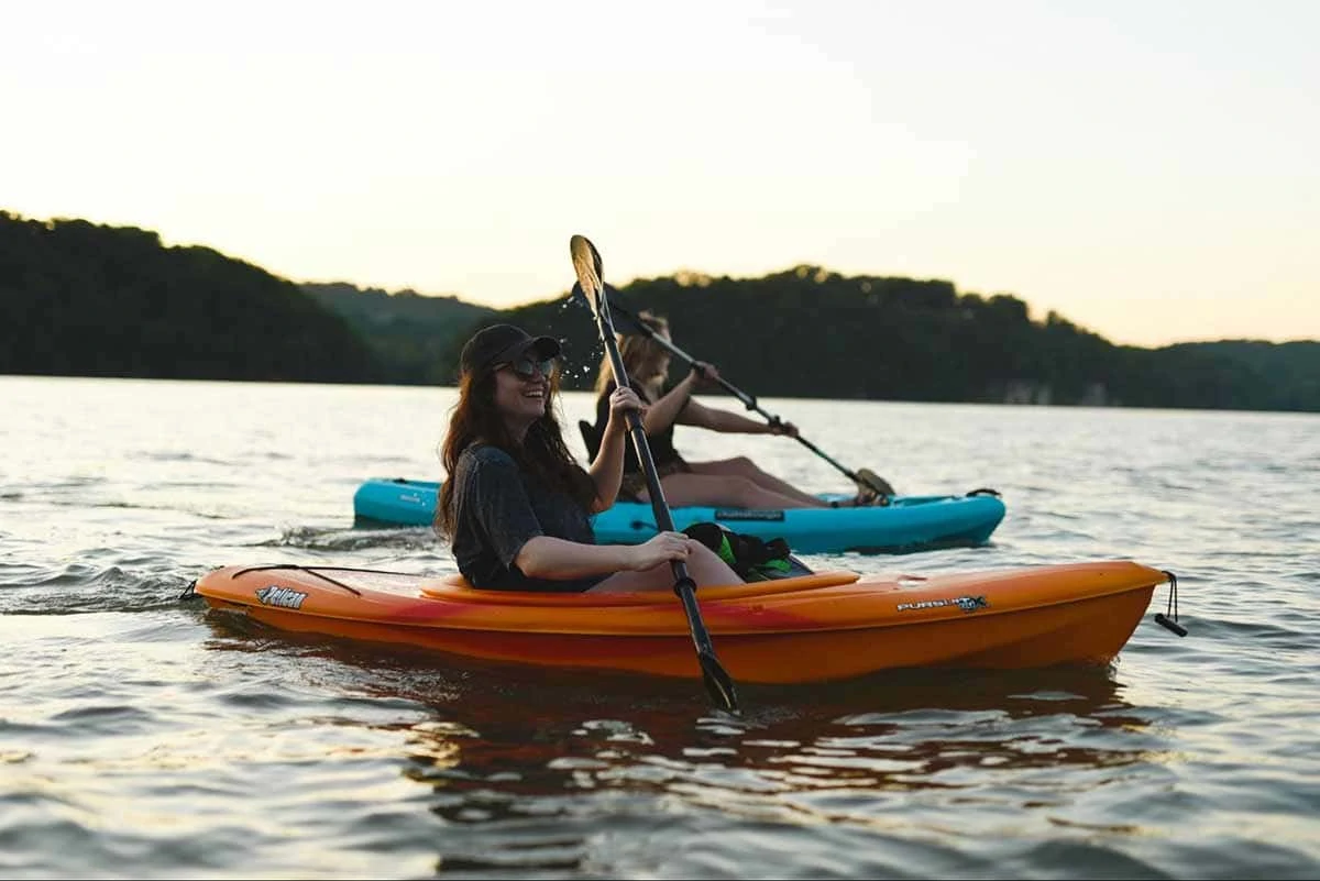 Image of two woman on two canoes in the ocean. There is an island in the background.