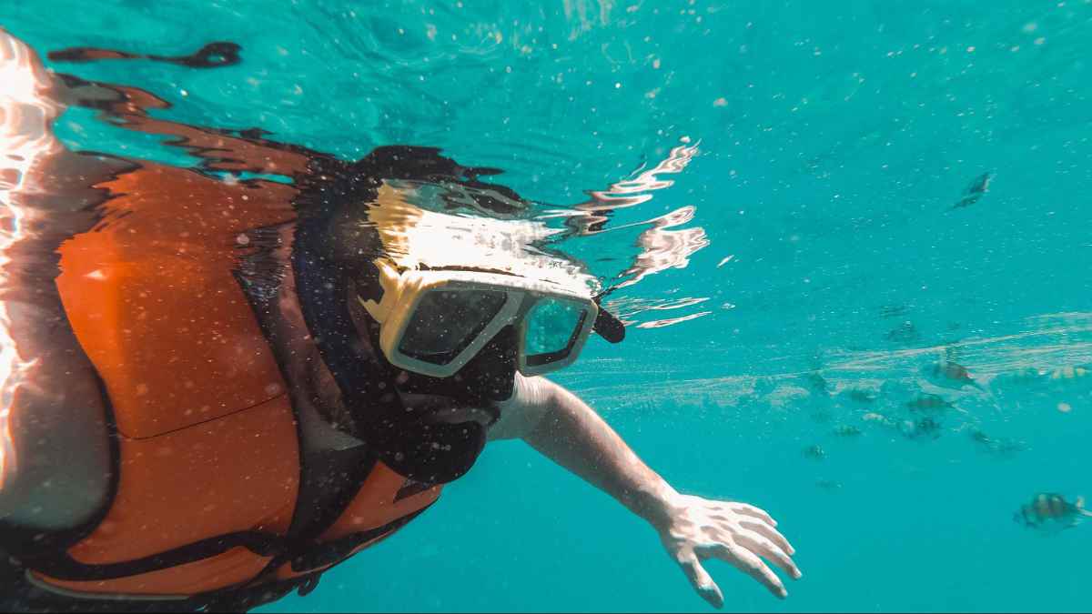 Man swimming with snorkeling gear in the ocean. The water is a beautiful turquoise blue.